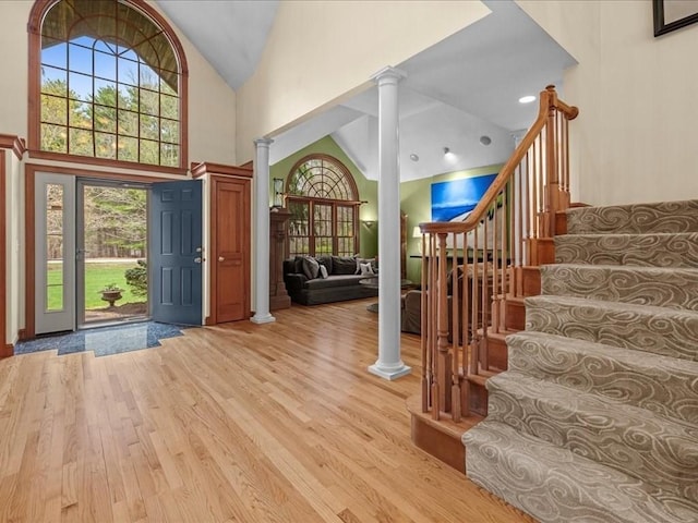 entrance foyer with stairs, ornate columns, high vaulted ceiling, and light wood-style flooring