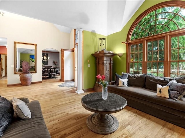 living room with arched walkways, high vaulted ceiling, baseboards, decorative columns, and wood finished floors