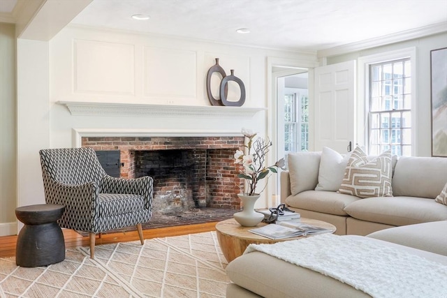 living area with light wood finished floors, a brick fireplace, and crown molding