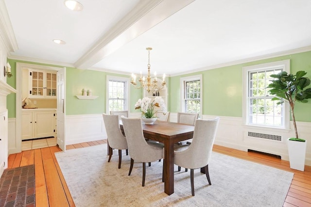 dining space with wainscoting, crown molding, an inviting chandelier, and wood-type flooring