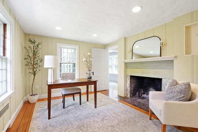 office space featuring plenty of natural light, wood finished floors, a fireplace with flush hearth, and a decorative wall