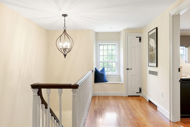 hall with an upstairs landing, an inviting chandelier, light wood finished floors, and baseboards