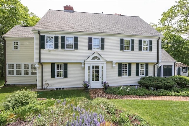 colonial-style house with a chimney, a front lawn, and a shingled roof