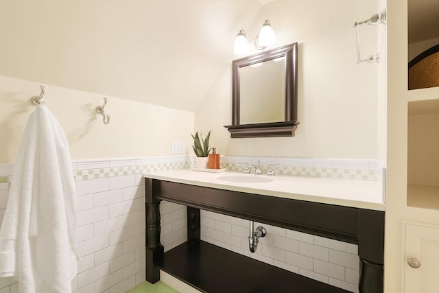 bathroom featuring a sink, a wainscoted wall, tile walls, and vaulted ceiling