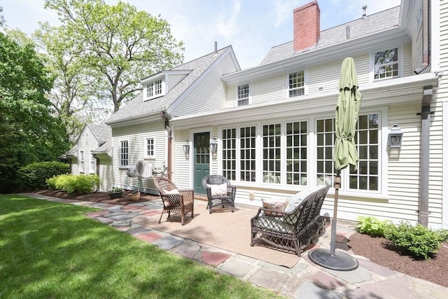 rear view of property with a yard, a shingled roof, a chimney, and a patio area