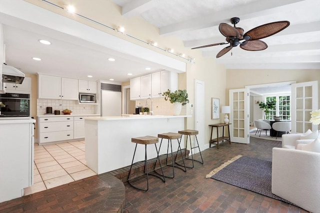 kitchen featuring french doors, a peninsula, brick floor, decorative backsplash, and built in appliances