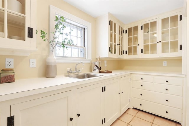 kitchen with glass insert cabinets, light countertops, light tile patterned floors, white cabinets, and a sink