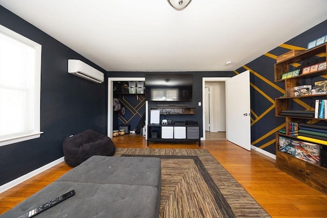 living area with an AC wall unit, wood finished floors, an accent wall, and baseboards