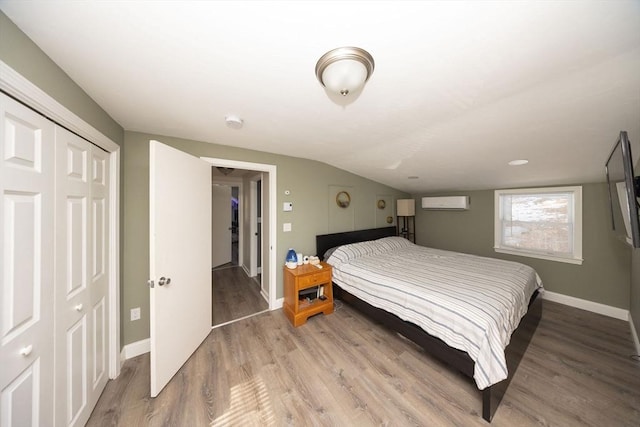 bedroom with light wood finished floors, baseboards, a closet, and a wall mounted AC