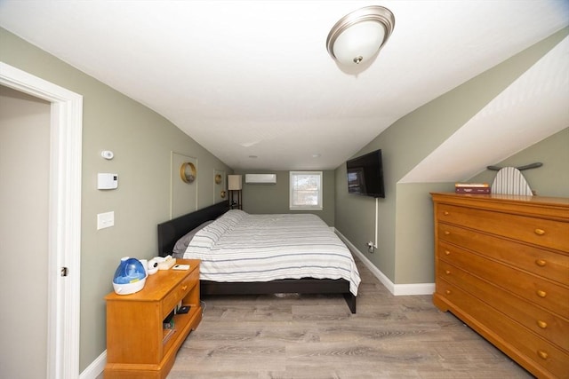 bedroom featuring lofted ceiling, a wall mounted air conditioner, light wood-style flooring, and baseboards