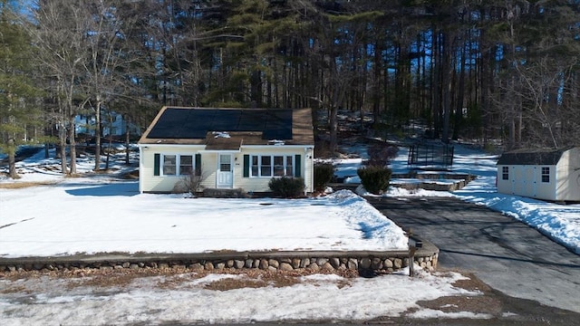 view of front facade featuring driveway, a storage shed, solar panels, and an outbuilding