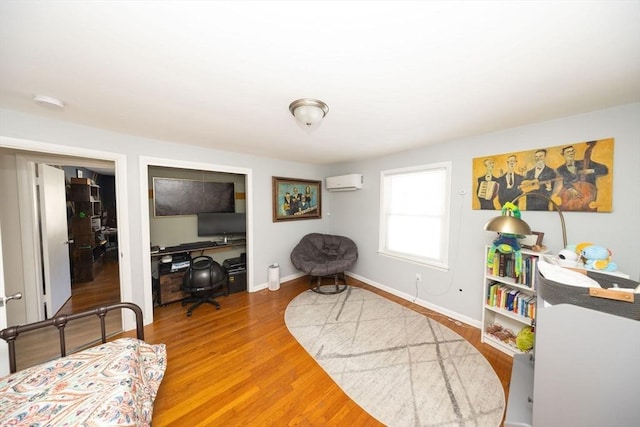 sitting room with baseboards, an AC wall unit, and wood finished floors