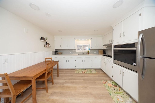 kitchen with appliances with stainless steel finishes, white cabinets, a sink, and wainscoting