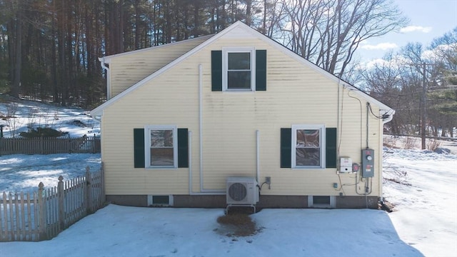 snow covered rear of property featuring ac unit and fence