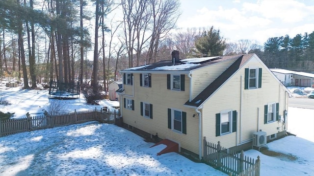 snow covered property featuring fence private yard, a chimney, and solar panels