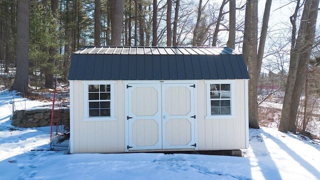 snow covered structure with a storage shed and an outbuilding