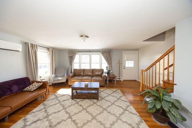 living room featuring stairway, a wall unit AC, wood finished floors, and a healthy amount of sunlight