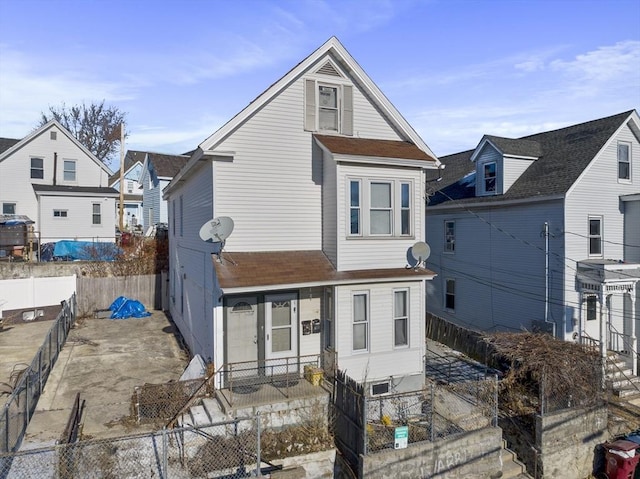rear view of property with a fenced front yard and roof with shingles