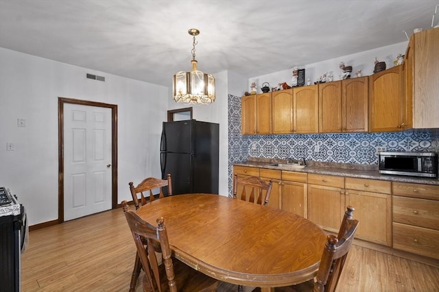 kitchen with stainless steel microwave, freestanding refrigerator, a chandelier, and light wood-style flooring