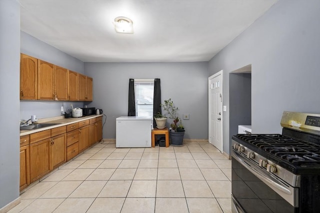 kitchen with stainless steel gas stove, fridge, light countertops, a sink, and brown cabinets