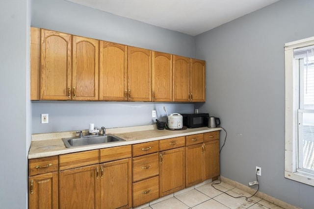 kitchen featuring a sink, black microwave, light countertops, brown cabinetry, and light tile patterned floors