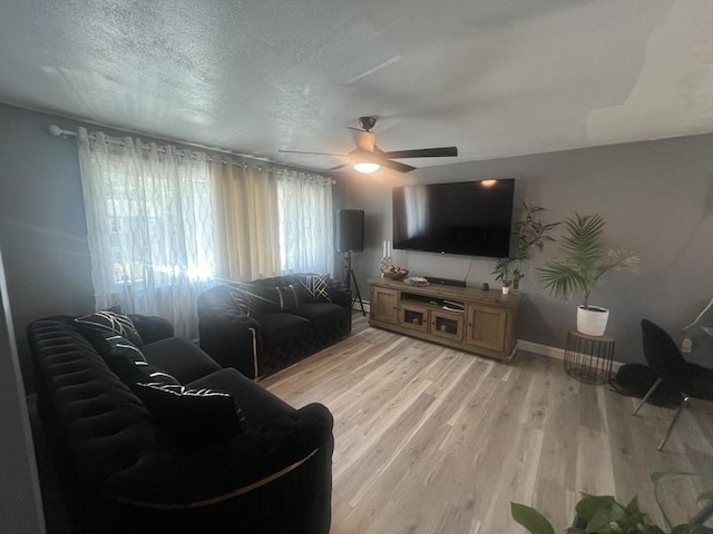 living room featuring a ceiling fan, baseboards, a textured ceiling, and light wood-style flooring