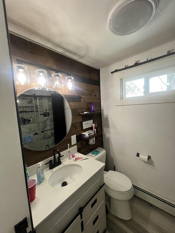 bathroom with wood finished floors, a baseboard heating unit, vanity, wooden walls, and toilet