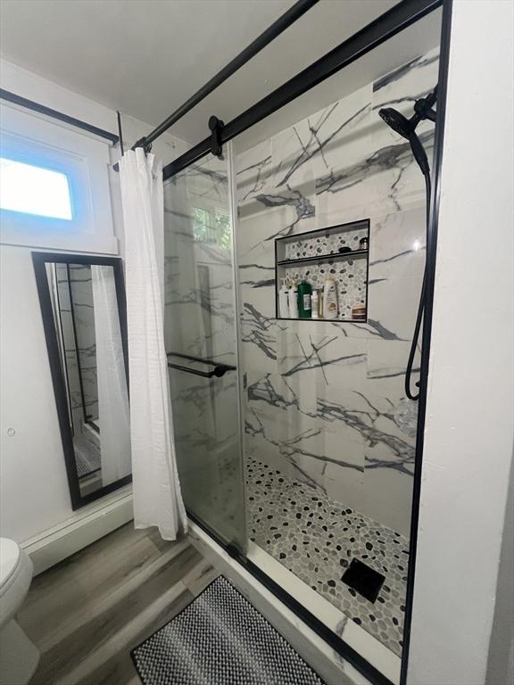 bathroom featuring toilet, wood finished floors, and a marble finish shower