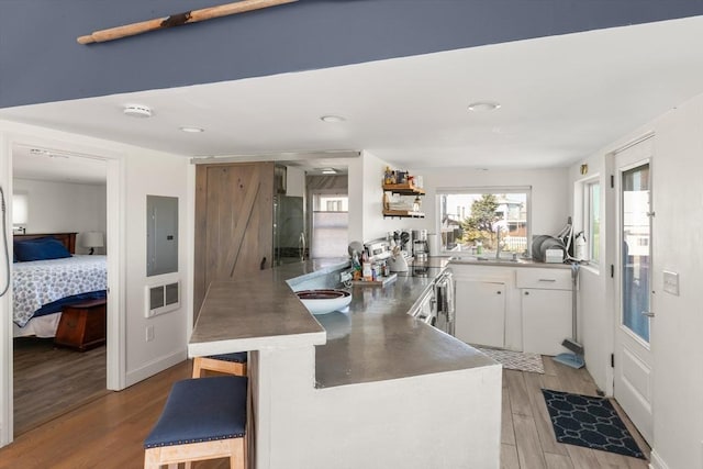 kitchen with white cabinets, a peninsula, light wood-type flooring, refrigerator, and electric panel