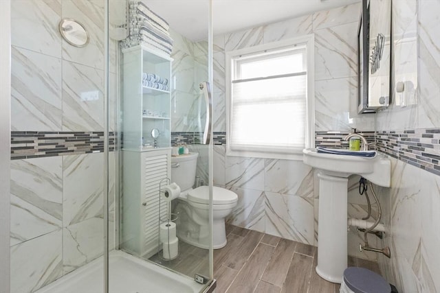 bathroom with toilet, tile walls, wood finished floors, and a stall shower