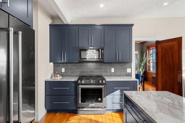 kitchen with stainless steel appliances, tasteful backsplash, light stone countertops, radiator, and light hardwood / wood-style flooring