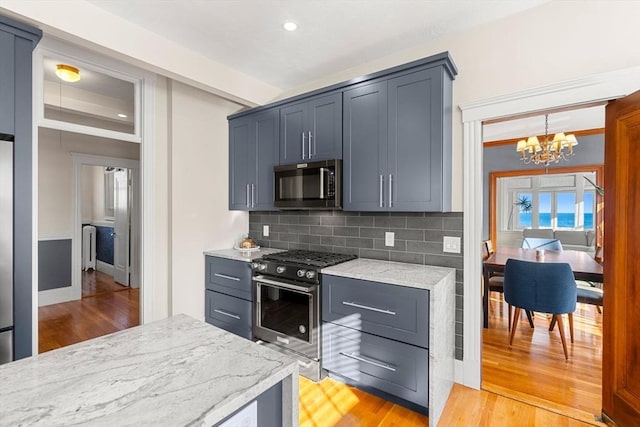 kitchen featuring stainless steel appliances, tasteful backsplash, a notable chandelier, light stone countertops, and light hardwood / wood-style flooring