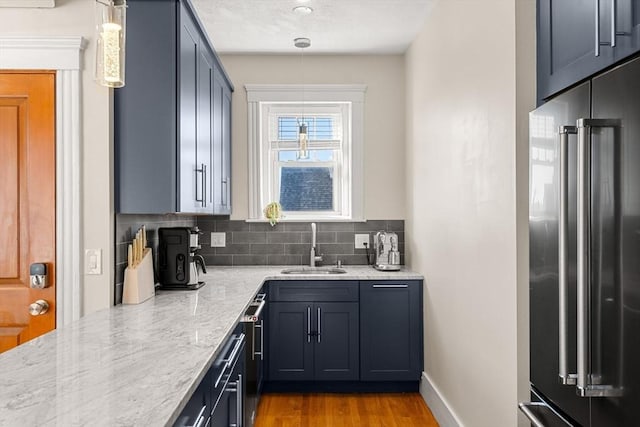 kitchen featuring tasteful backsplash, high end refrigerator, hanging light fixtures, light stone counters, and sink