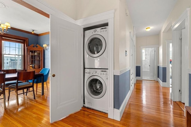 clothes washing area featuring stacked washer / dryer, an inviting chandelier, crown molding, and light hardwood / wood-style floors