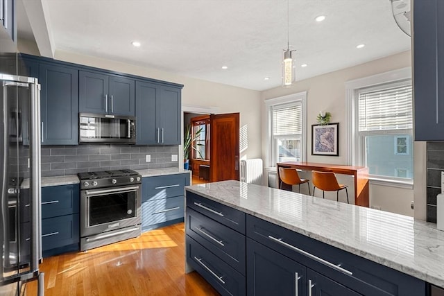 kitchen featuring appliances with stainless steel finishes, decorative light fixtures, tasteful backsplash, light hardwood / wood-style floors, and blue cabinetry