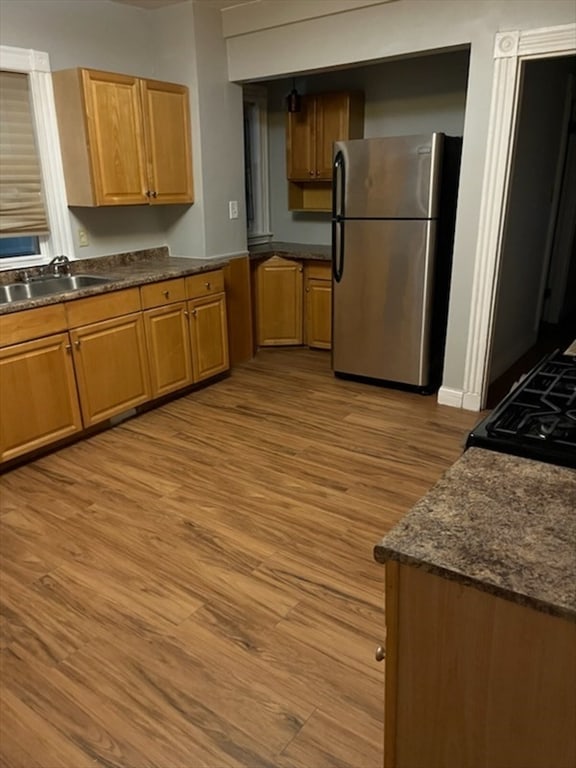 kitchen with dark stone counters, stainless steel fridge, sink, and light hardwood / wood-style flooring