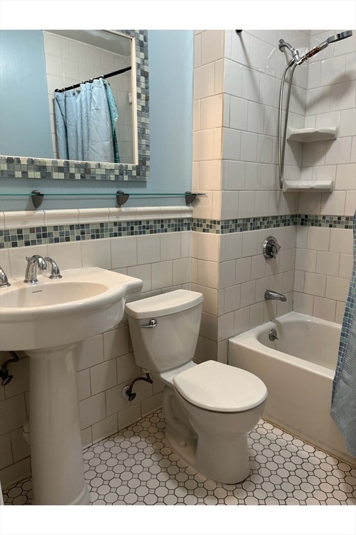 bathroom featuring shower / bath combination with curtain, tile patterned floors, toilet, and tile walls