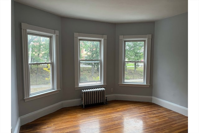 spare room featuring radiator, hardwood / wood-style floors, and a healthy amount of sunlight