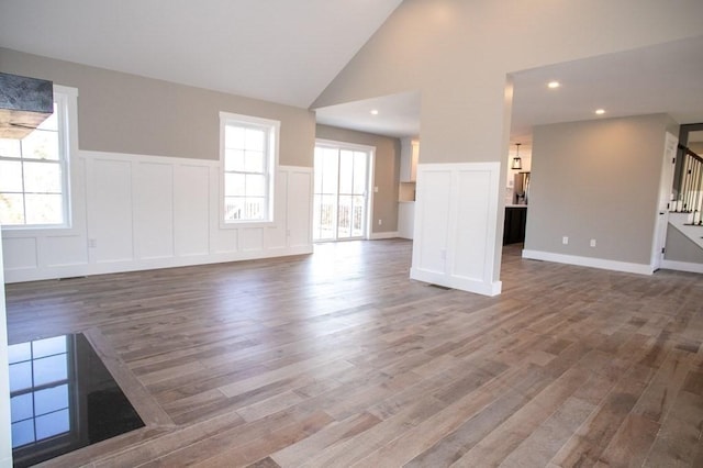 unfurnished living room with wood finished floors, a decorative wall, stairway, high vaulted ceiling, and plenty of natural light
