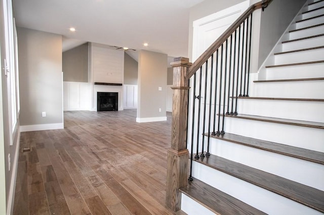 stairway featuring wood finished floors, baseboards, recessed lighting, and a fireplace