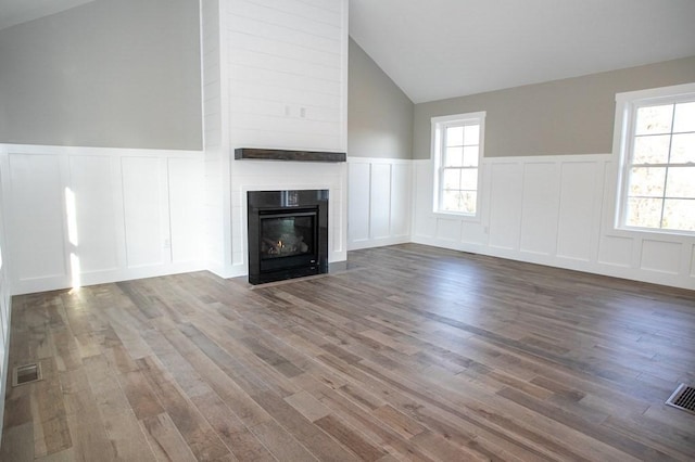 unfurnished living room with a decorative wall, lofted ceiling, a wainscoted wall, wood finished floors, and healthy amount of natural light