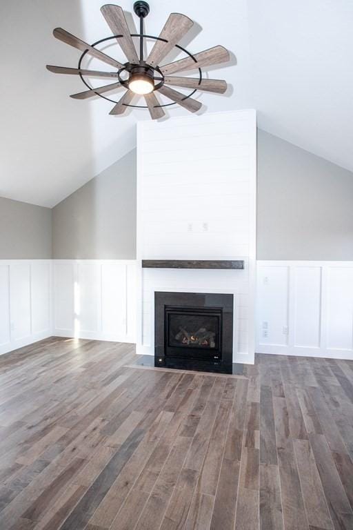unfurnished living room featuring lofted ceiling, a decorative wall, a wainscoted wall, wood finished floors, and a fireplace