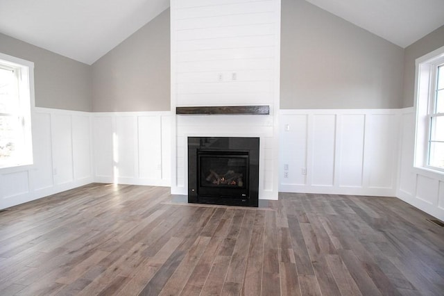 unfurnished living room featuring a decorative wall, vaulted ceiling, wood finished floors, a wainscoted wall, and a fireplace with flush hearth