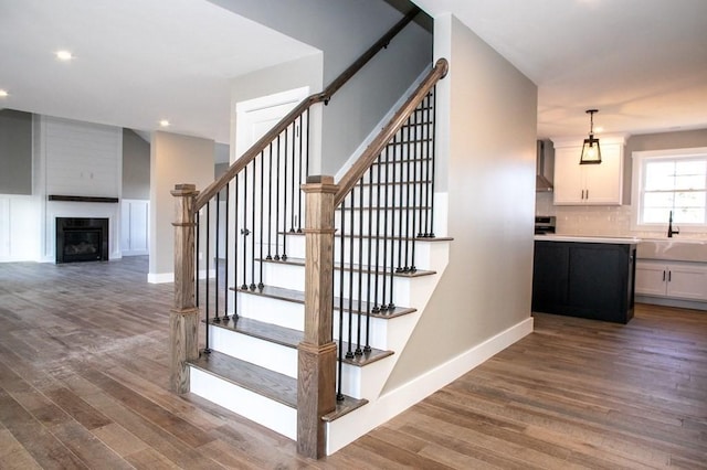 stairs featuring wood finished floors, baseboards, recessed lighting, and a large fireplace
