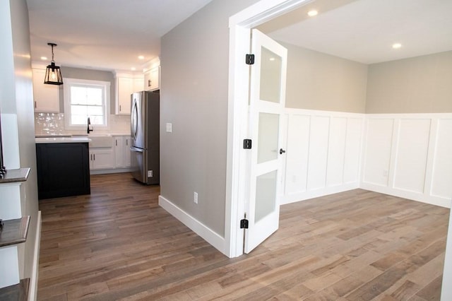 hallway featuring wood finished floors, a decorative wall, recessed lighting, a wainscoted wall, and a sink