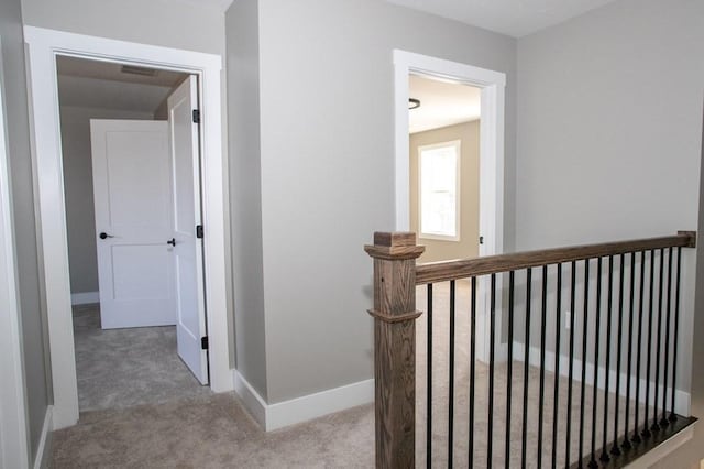 hall featuring carpet flooring, baseboards, and an upstairs landing