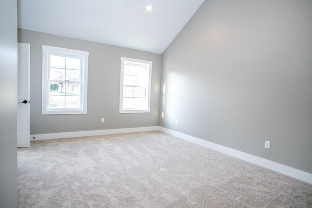 empty room with vaulted ceiling, light carpet, and baseboards