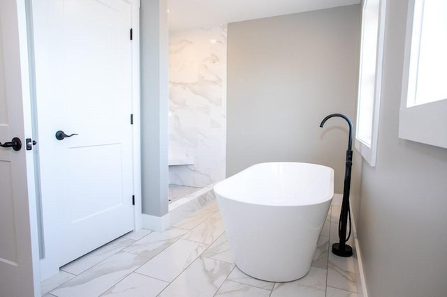 bathroom with marble look tile flooring, a freestanding tub, a shower stall, and baseboards