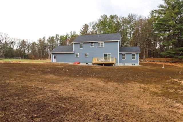 rear view of house with a deck, view of wooded area, and a shingled roof