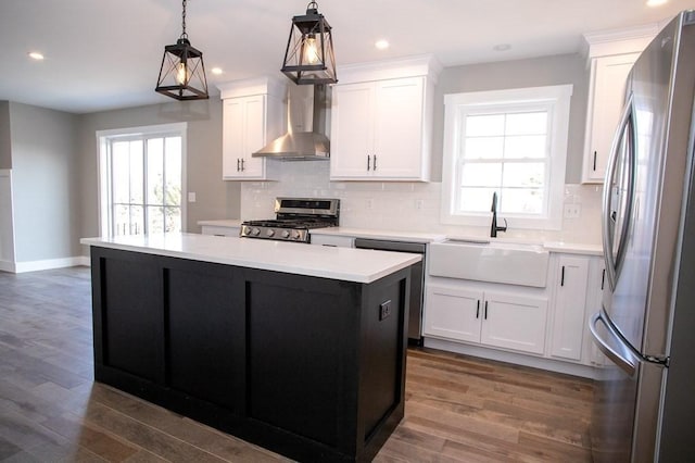 kitchen featuring appliances with stainless steel finishes, a sink, wall chimney range hood, a center island, and tasteful backsplash